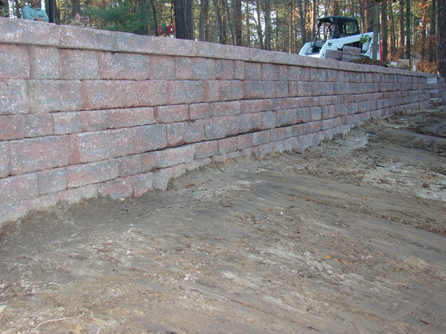 Brick retaining wall on graded sand, with a small construction vehicle in the background.