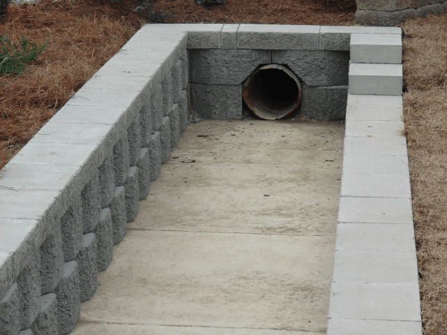 Concrete drainage channel with a pipe outlet in a dry, outdoor setting.