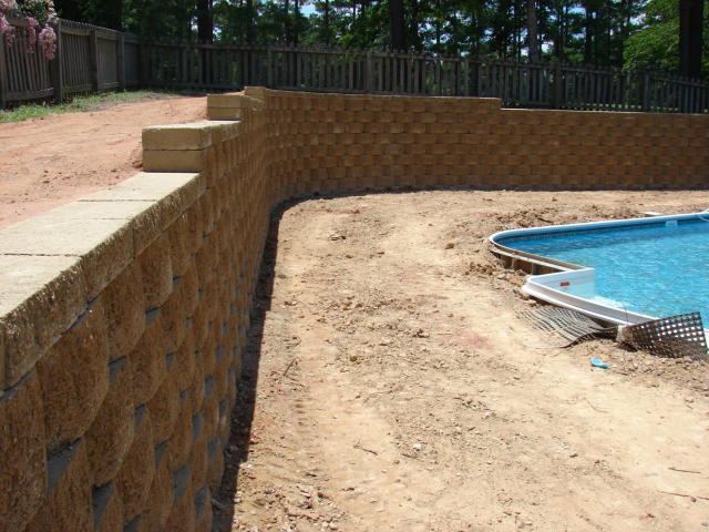 Retaining walls made of tan blocks surround a dirt area and pool.