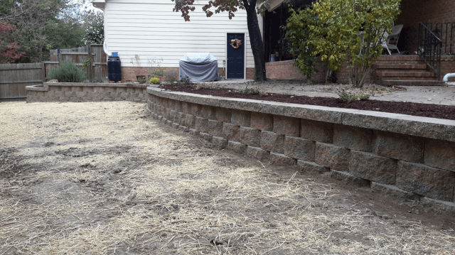 A yard with retaining walls made of stone blocks, and a house in the background.