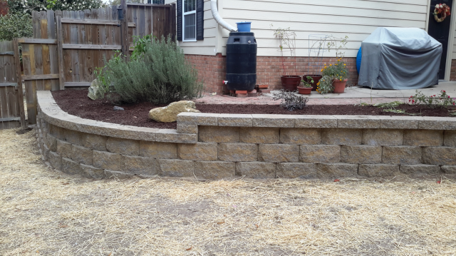 Stone retaining wall with a landscaped garden bed against a house and fence.