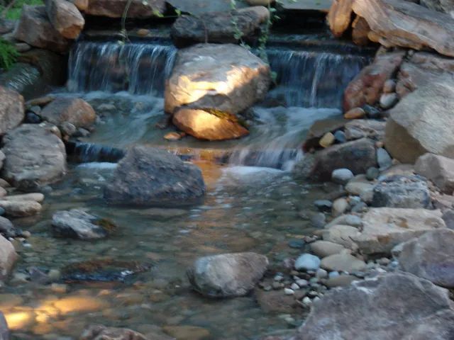 Small waterfall cascading over rocks into a stream, lit by soft golden lights.