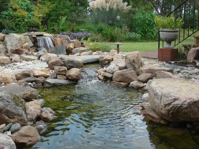 A water garden with a waterfall, rocks, and green foliage. Water ripples.