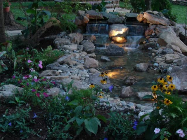Water feature with a small waterfall, rocks, and colorful flowers.
