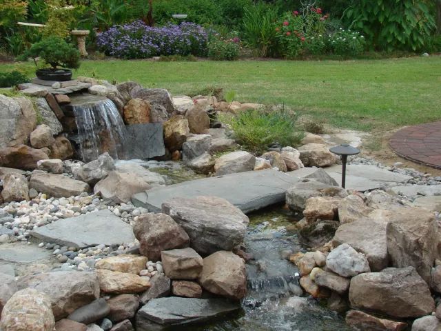 A backyard with a small waterfall feature flowing over rocks into a pond.