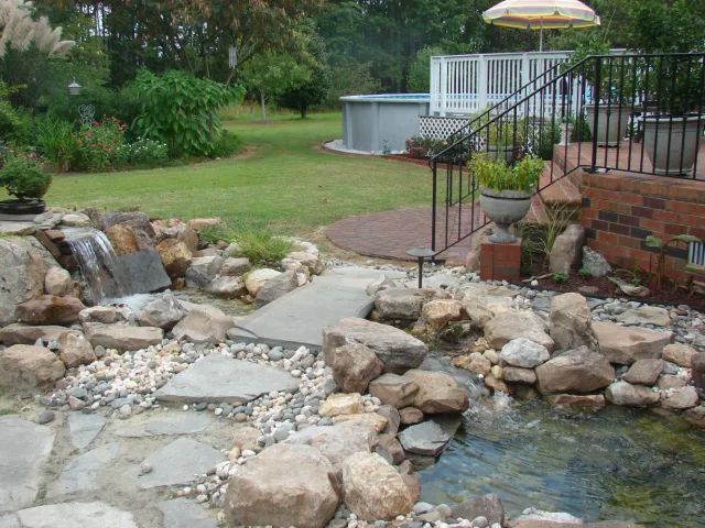 Backyard with a water feature, including a small waterfall, rocks, and a raised pool.