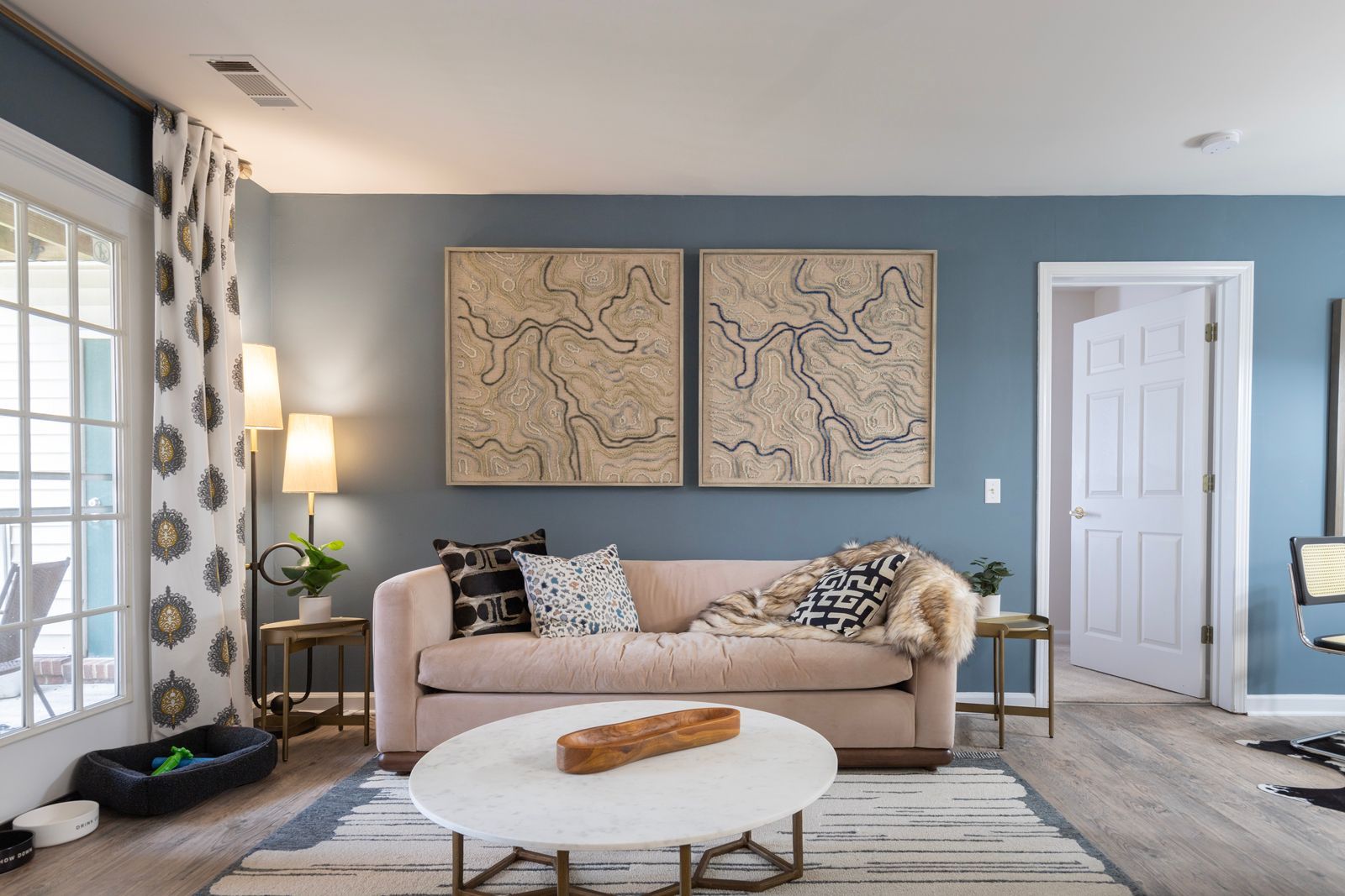 A living room with a couch , coffee table , and two paintings on the wall.