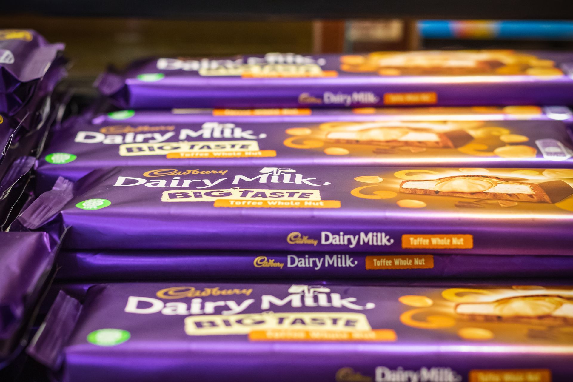 Several Cadbury Dairy Milk Big Taste chocolate bars stacked on a shelf; purple packaging.