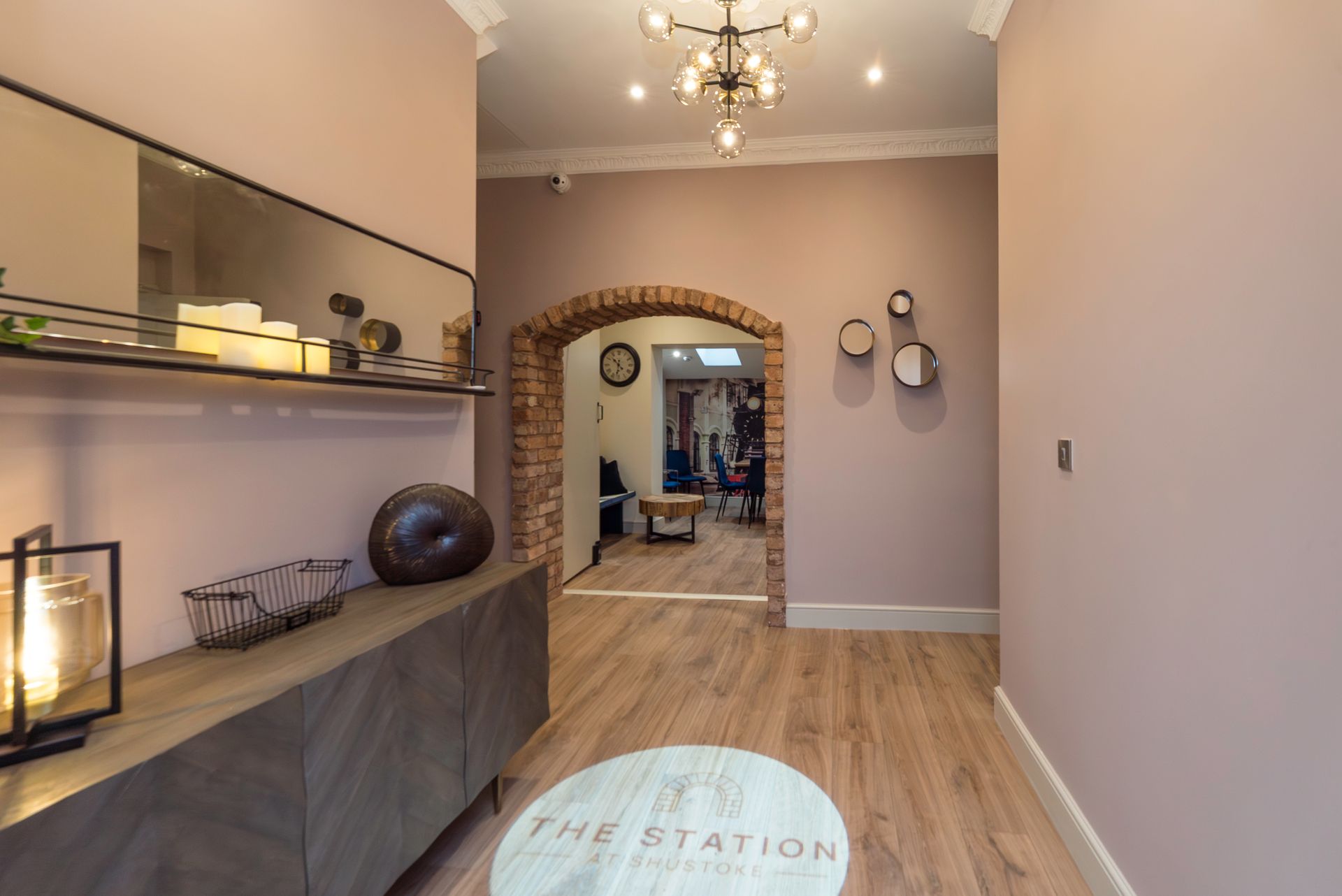 Hallway with pink walls, wooden floor, and an arched brick doorway leading to another room.
