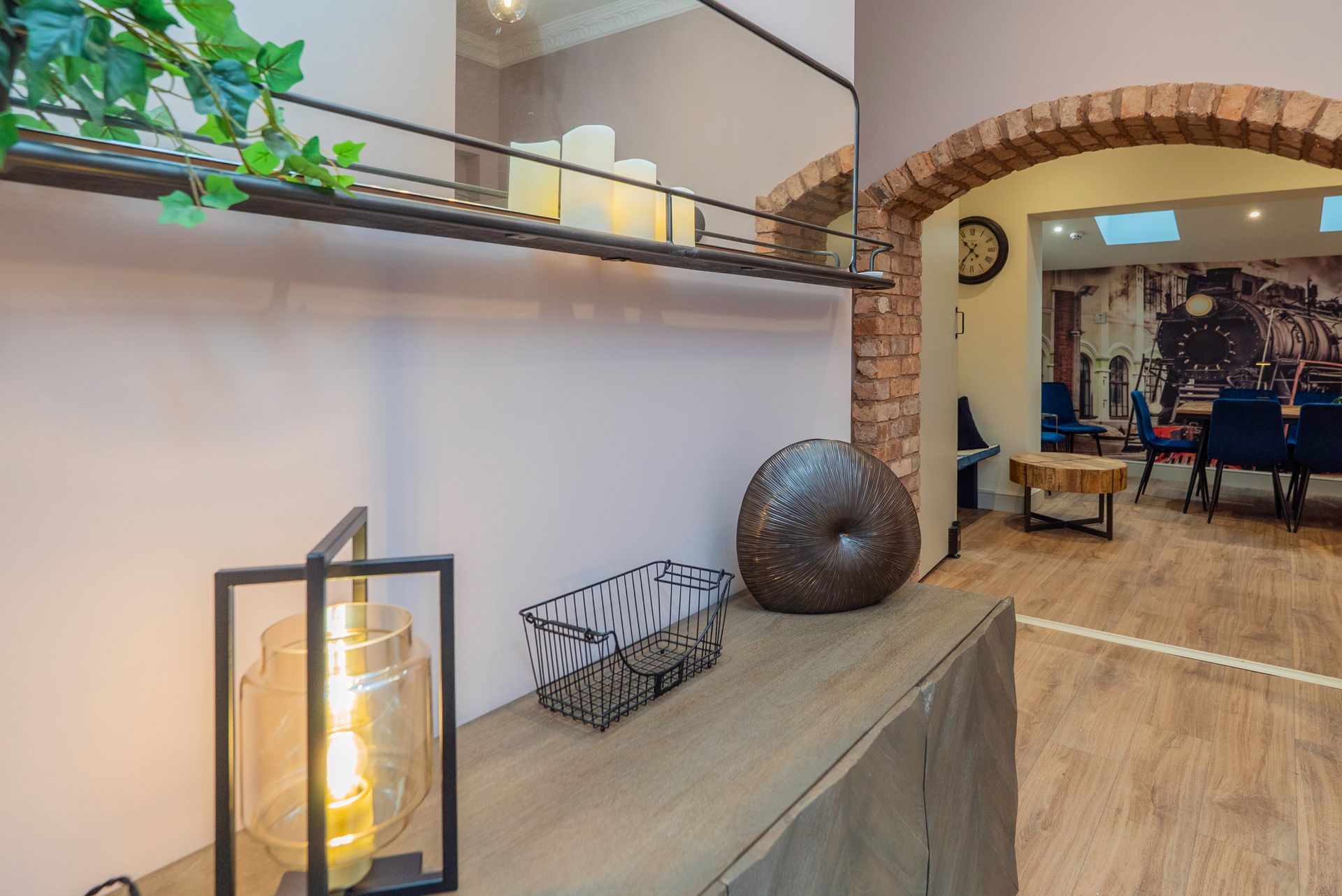 A console table with decor, a lamp, and a mirror next to an arched doorway.
