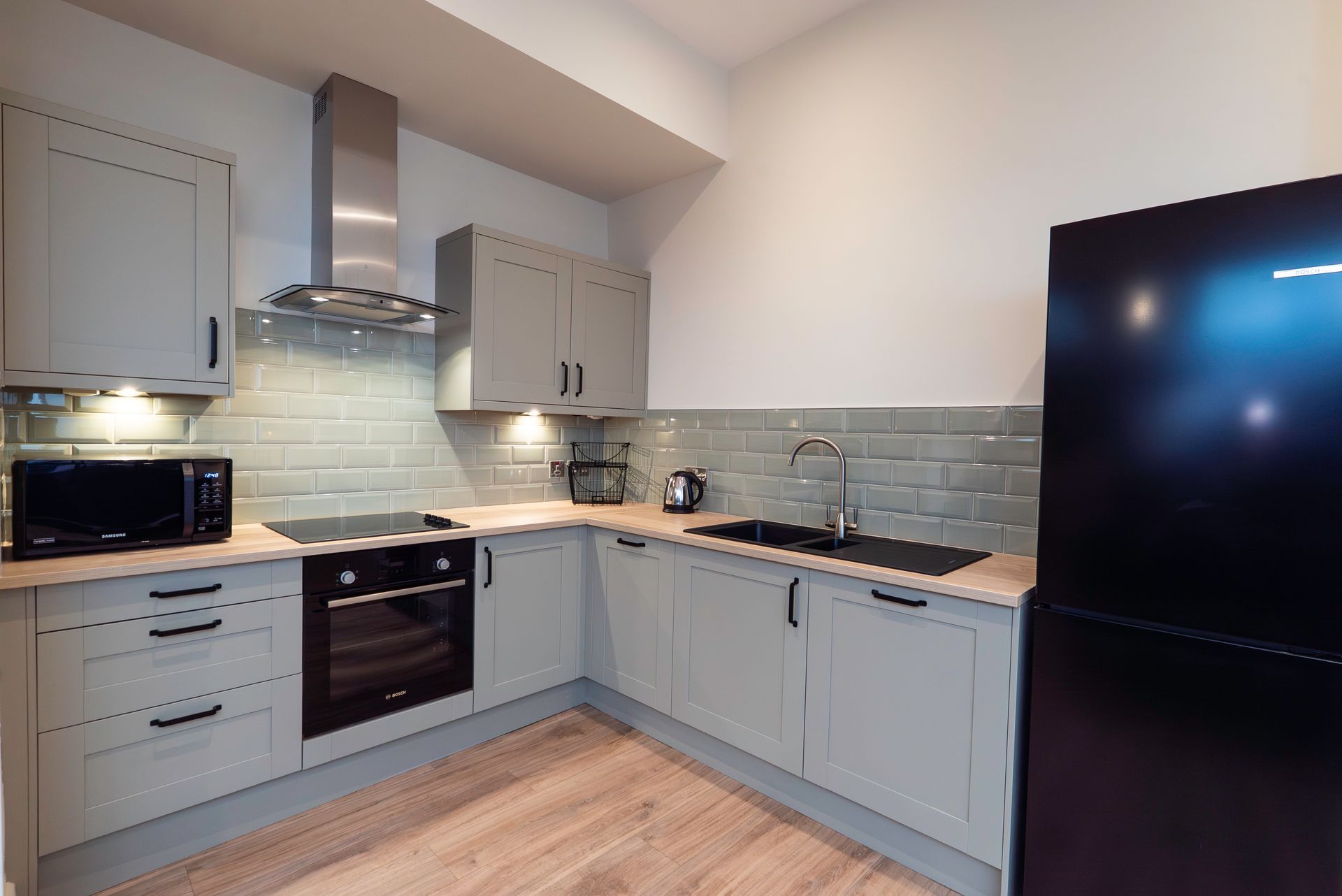 Gray kitchen with wood countertops, black appliances, and green tile backsplash.