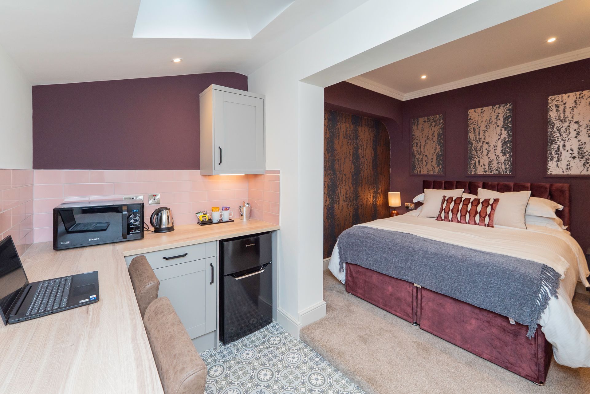 Small apartment interior with kitchen, desk, and bedroom; purple and gray color scheme.