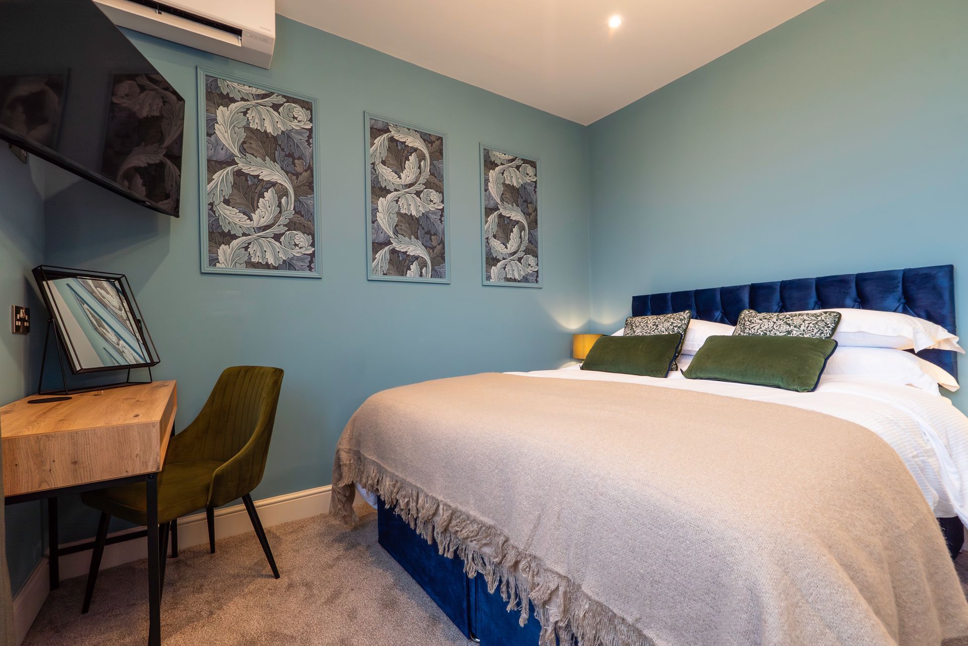 Bedroom with blue walls, bed, vanity, and decorative wall hangings.