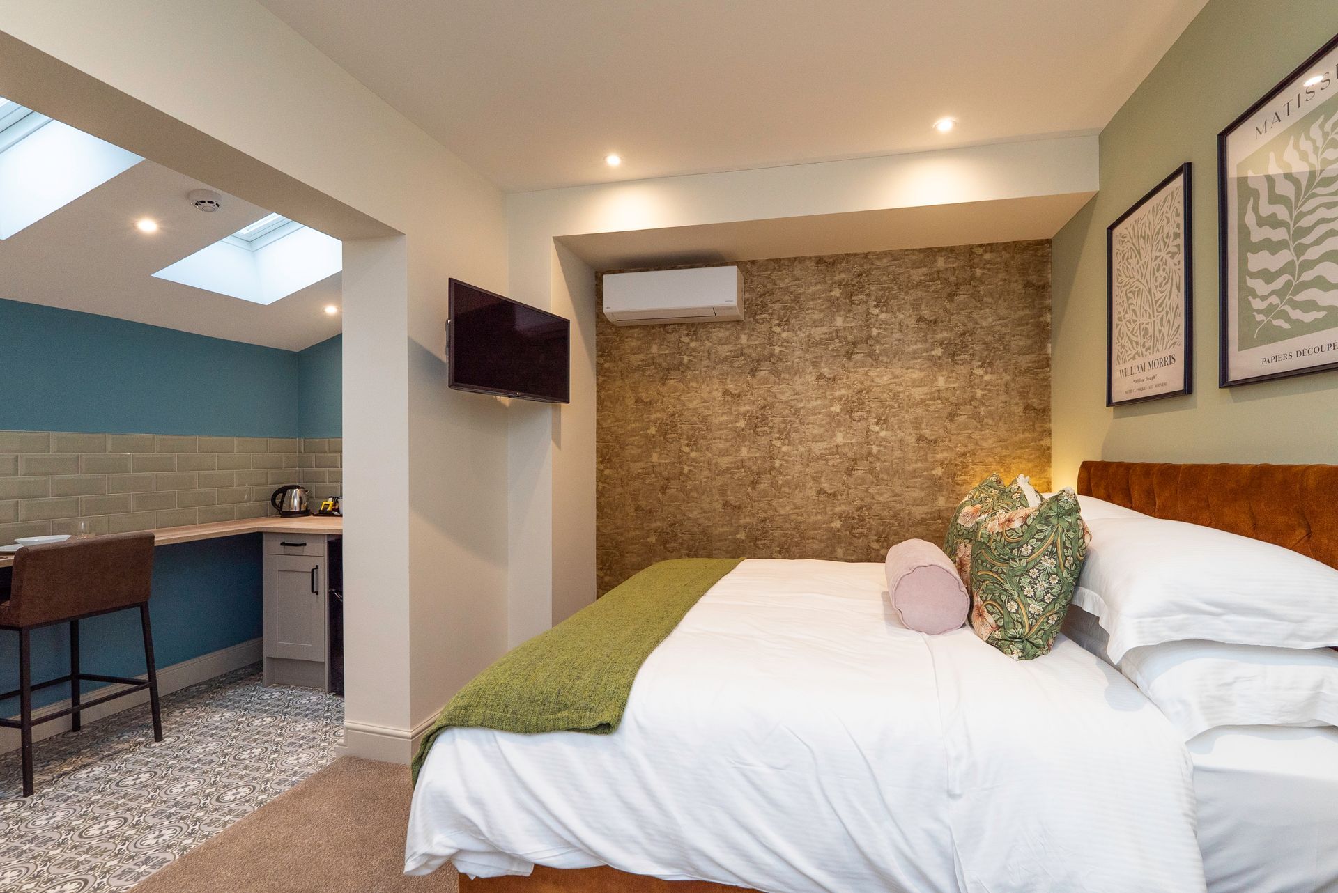 Bedroom with bed, kitchenette, TV, and decorative wall.