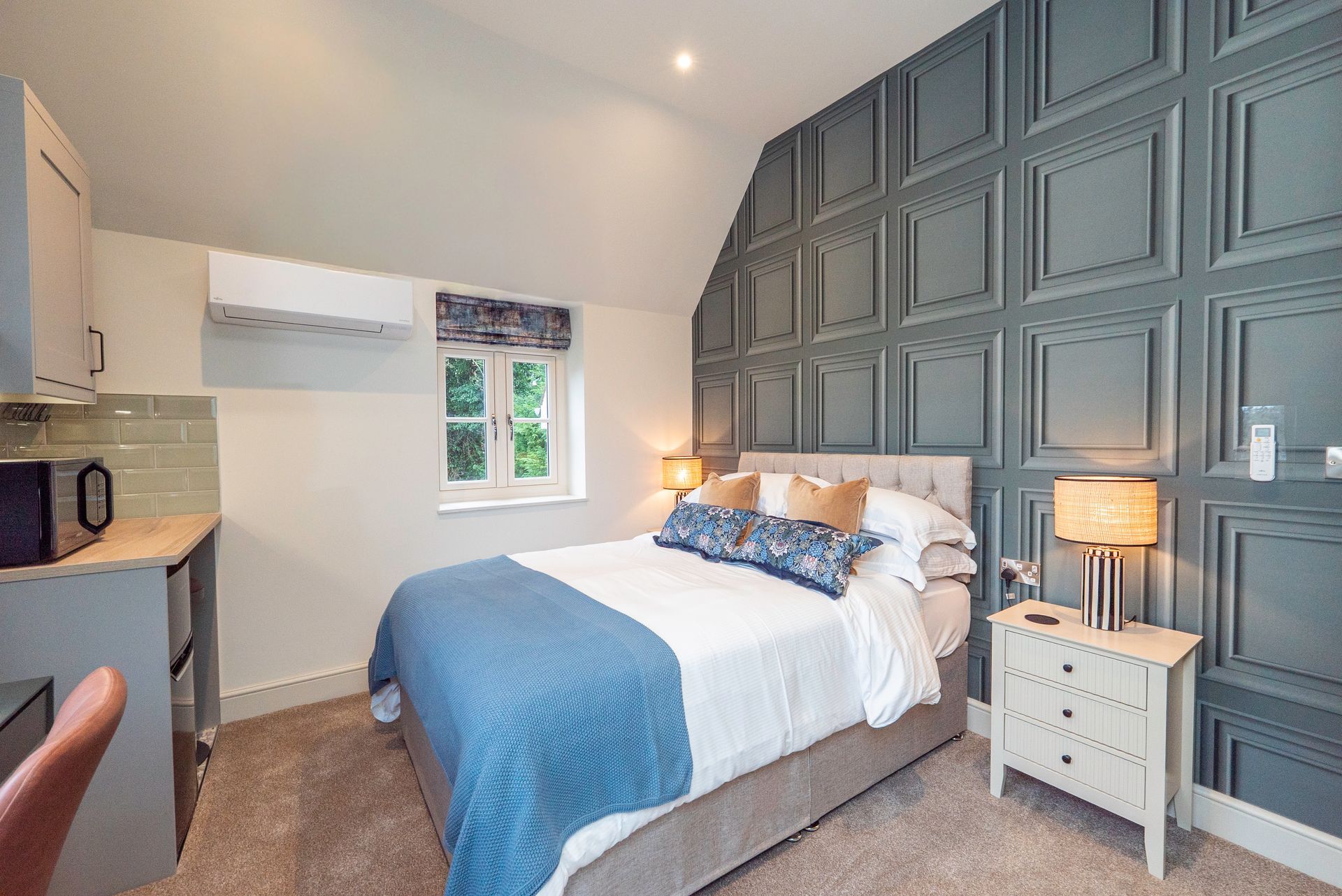 Bedroom with blue accent wall, double bed, small kitchenette, and window.
