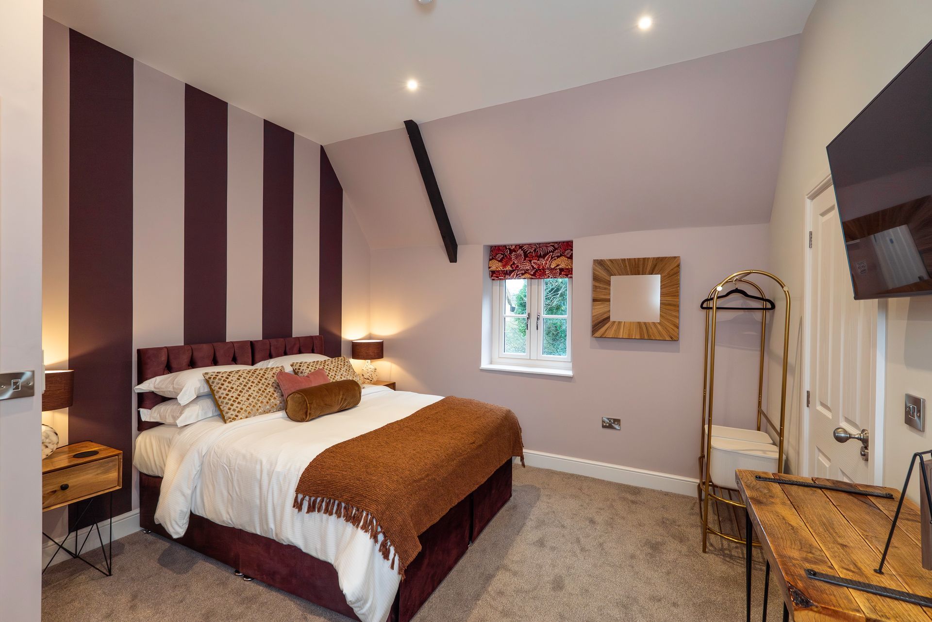Bedroom with a striped accent wall, bed, small window, and gold-toned furnishings.