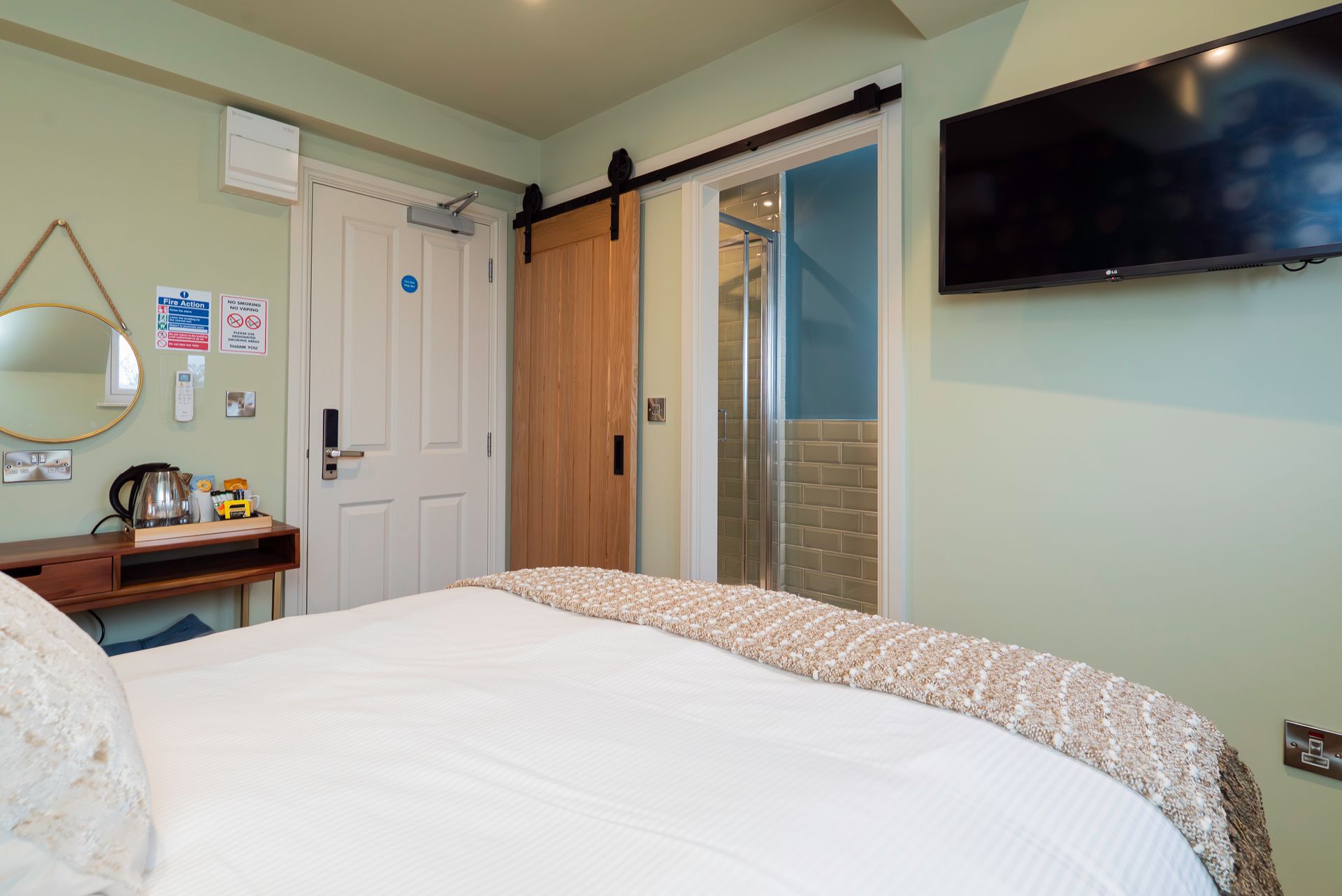 Bedroom with a bed, TV, wooden door, small table with a kettle, and a sliding door to the shower.