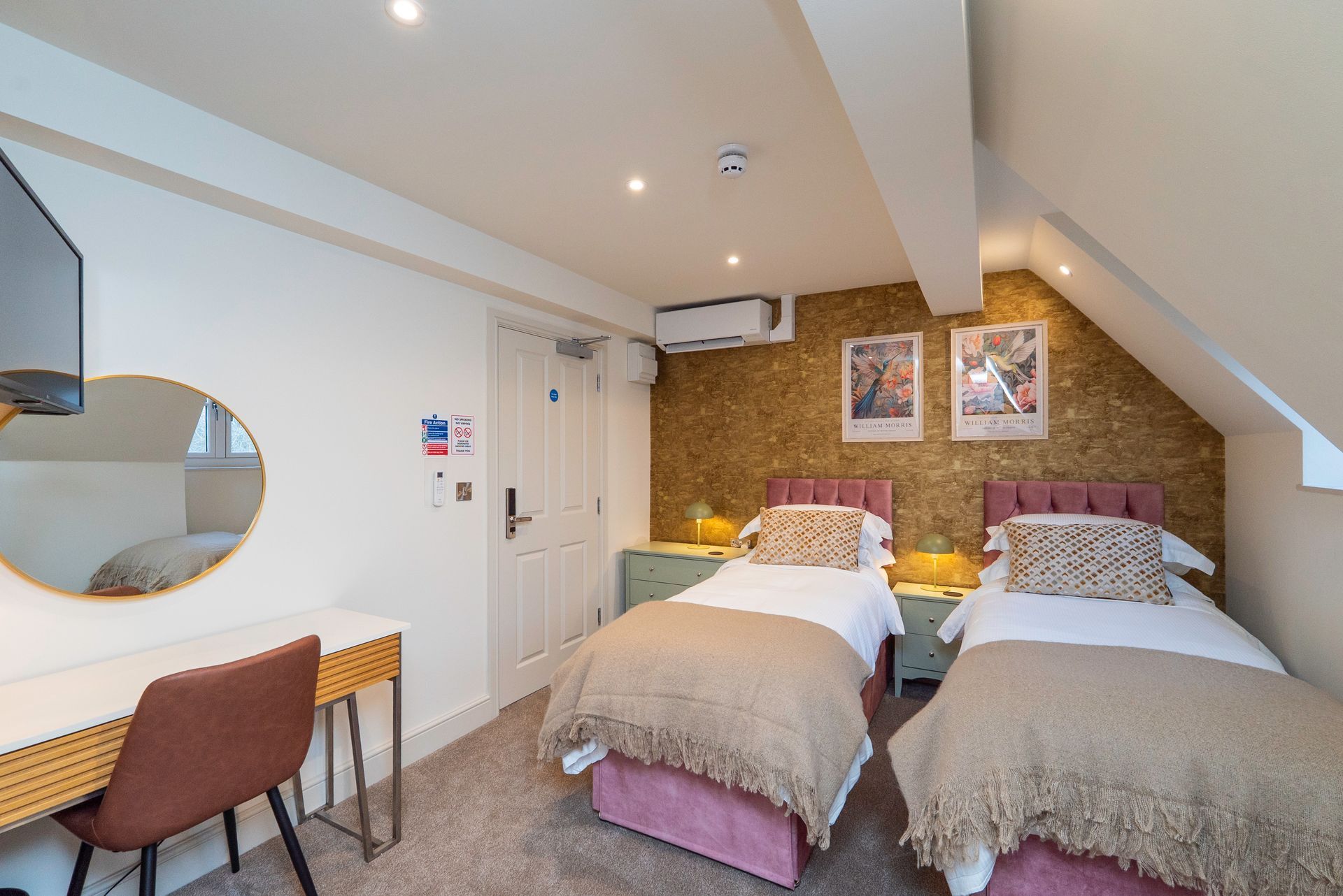 Twin bedroom with two beds, a desk, and a wall-mounted TV. The room has a neutral color scheme.