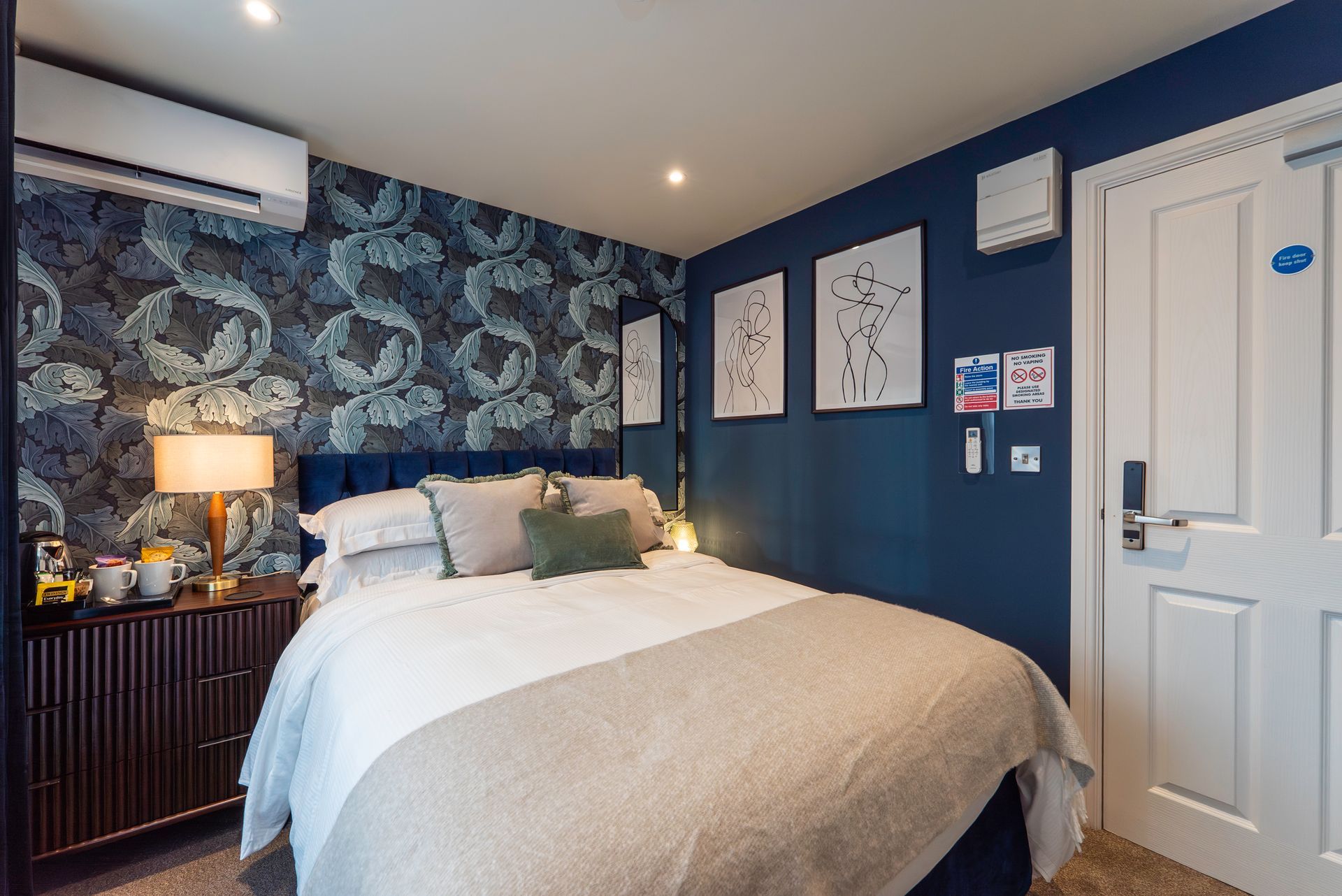 Bedroom with a patterned wallpaper wall, a bed with pillows and blanket, and a dark wooden dresser.