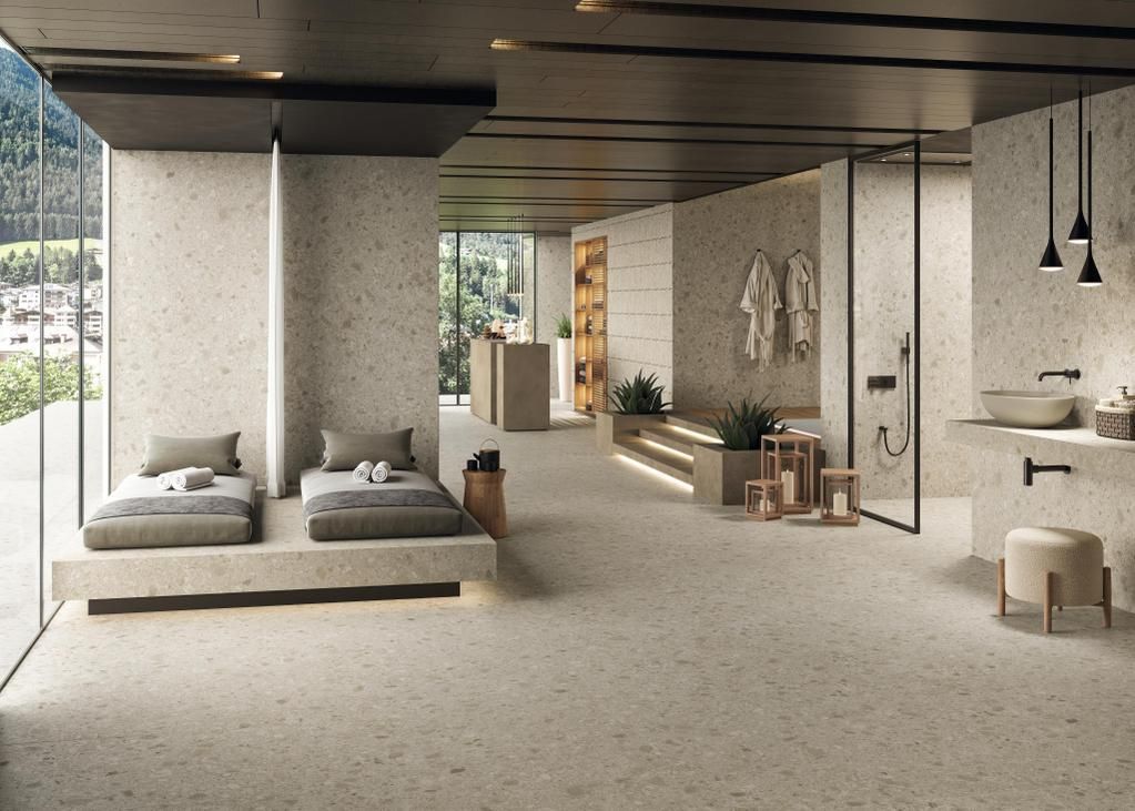 Una spa moderna dai toni neutri con due lettini prendisole, una zona doccia e arredi minimalisti sotto un soffitto a doghe scure.
