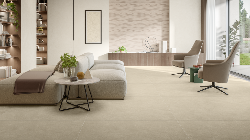 Un soggiorno moderno con pavimento piastrellato beige, un divano modulare neutro, un tavolino rotondo e due poltrone contemporanee.