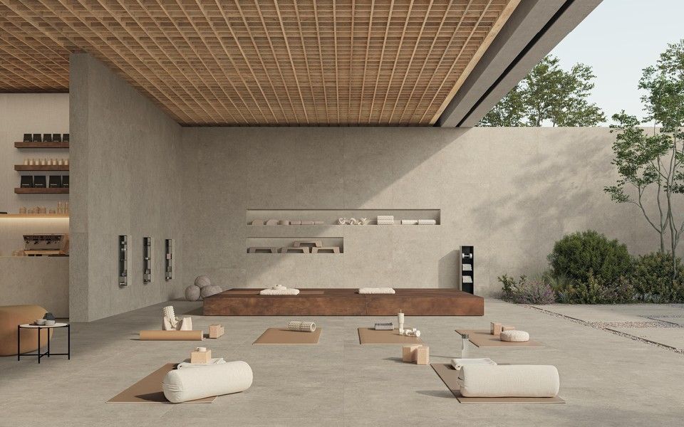 Studio di yoga minimalista con soffitto in legno, pareti in cemento neutro e tappetini da yoga disposti sul pavimento.