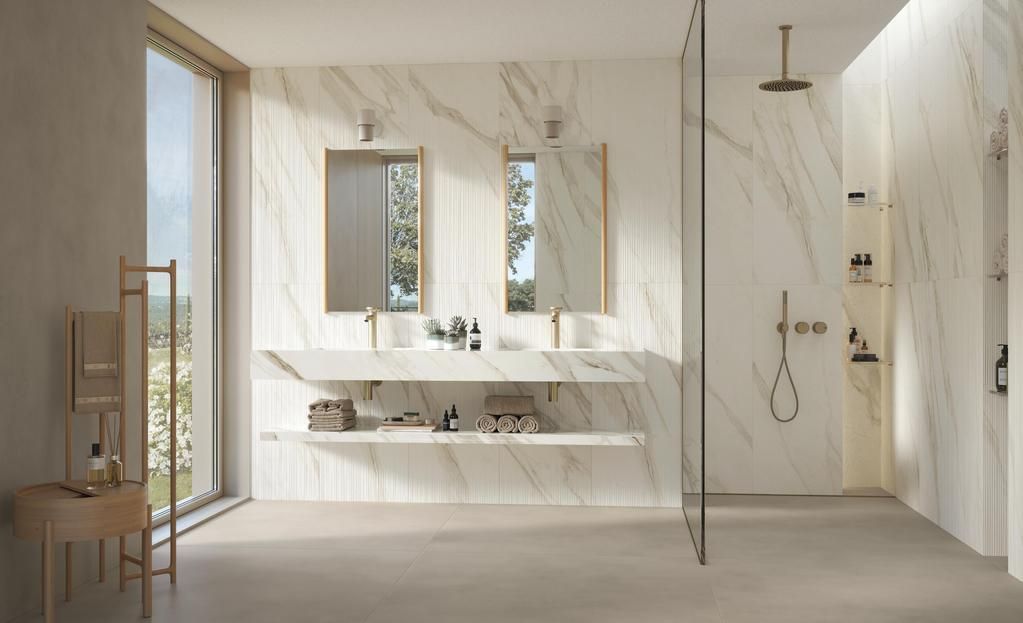 Un bagno moderno e minimalista con pareti in marmo bianco, doppio lavabo, rubinetteria dorata e cabina doccia con box in vetro.