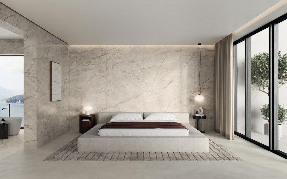 Una camera da letto minimalista con una parete in pietra beige, un letto a piattaforma basso, un tappeto a motivi geometrici e finestre a tutta altezza.
