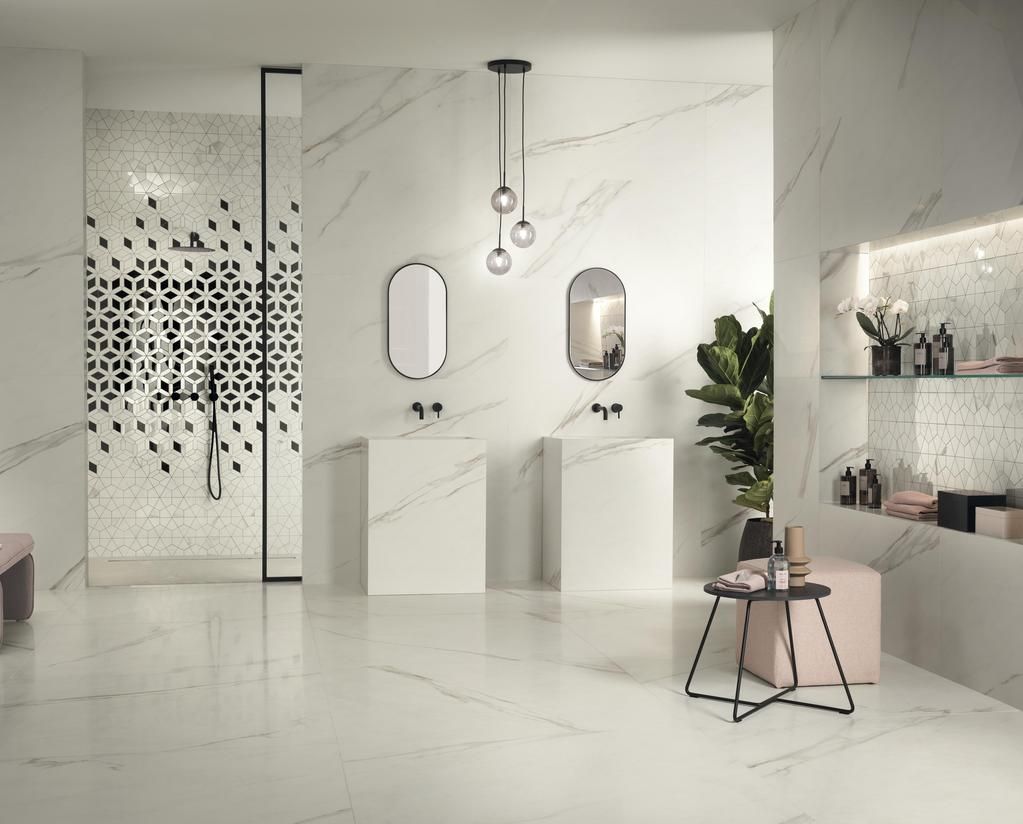 Bagno moderno con pareti e pavimento in marmo bianco, due specchi ovali, lavabi a colonna, doccia con design particolare e una pianta.