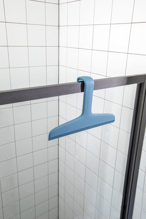 Un tergivetro da doccia in silicone blu agganciato al bordo superiore di una porta di vetro della doccia, contro una parete piastrellata.
