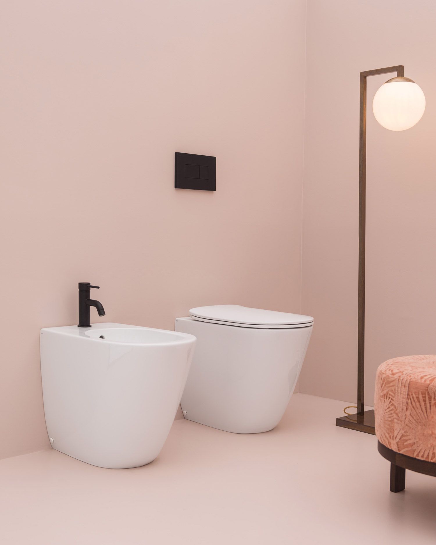 In un bagno moderno dai toni rosa, con lampada da terra, un bidet bianco e un WC sospeso con rubinetteria nera.