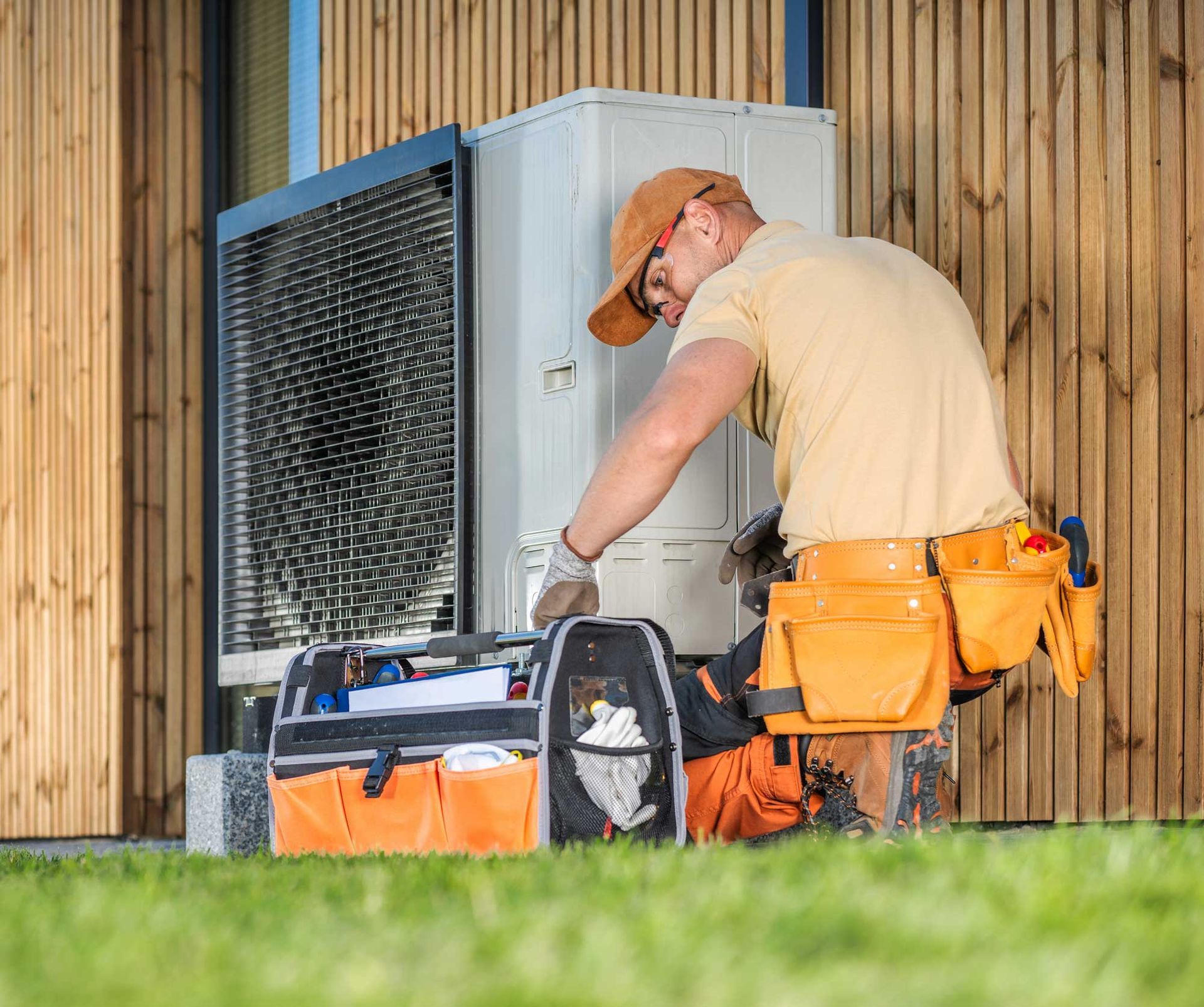 A male HVAC technician checks a heating pump installed on the side of a house.
