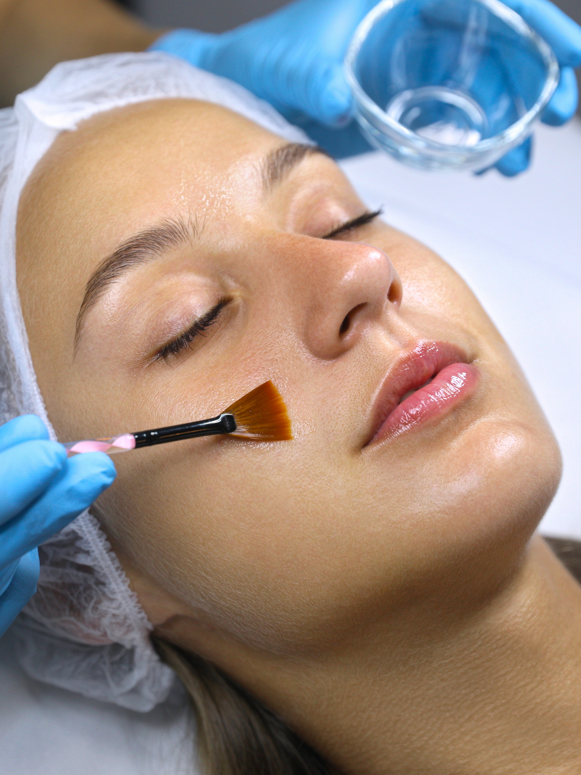 A woman is getting a facial treatment with a brush on her face.