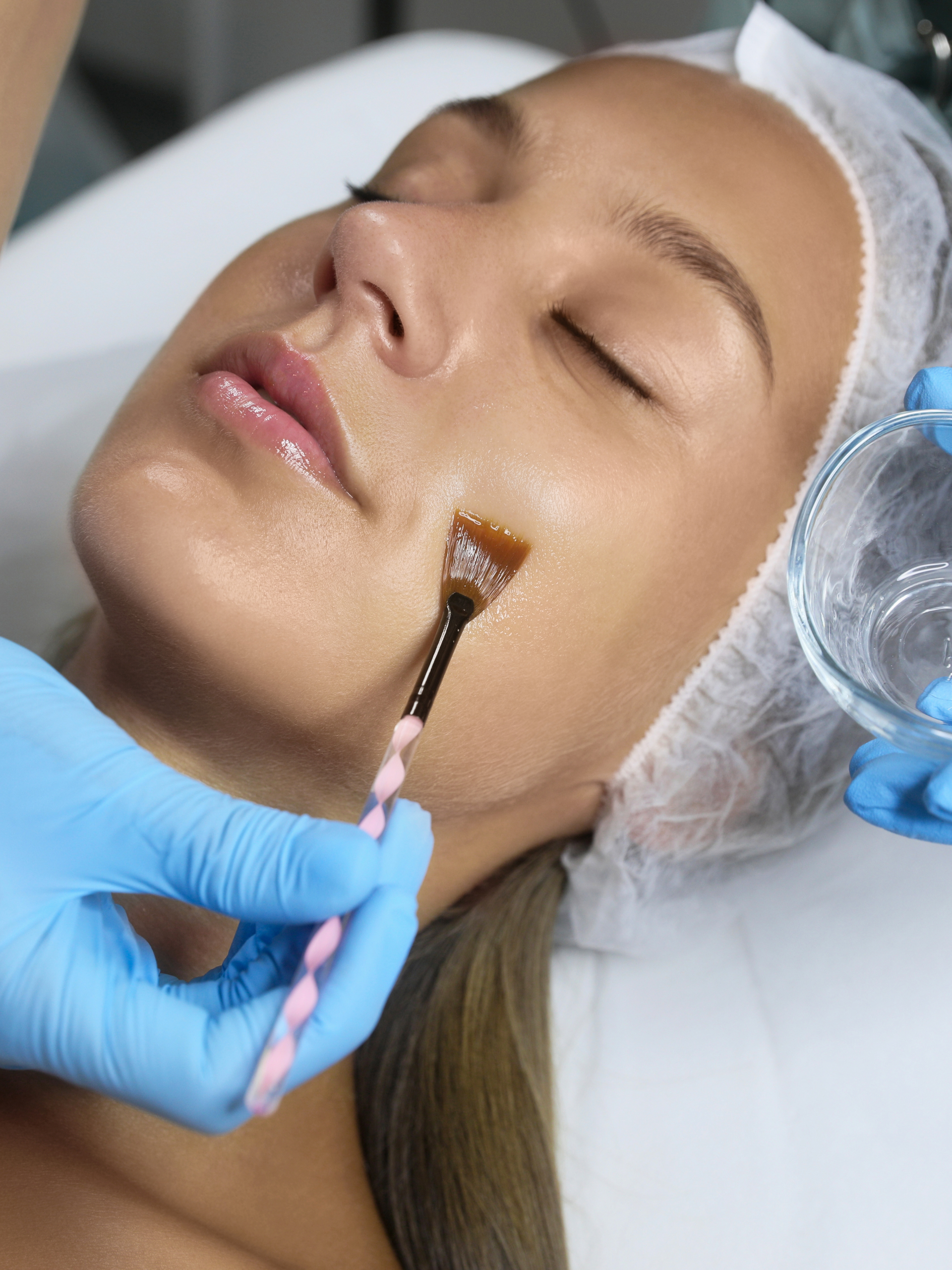 A woman is getting a facial treatment with a brush on her face.