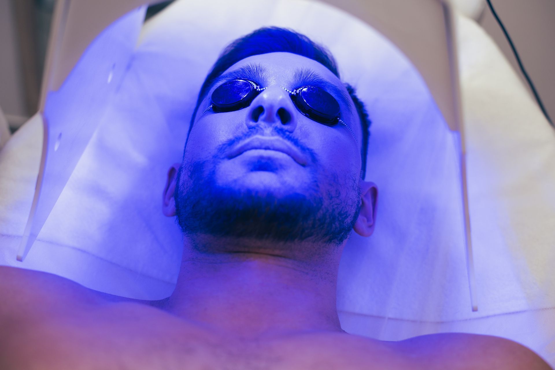 A man is laying on a bed with a blue light on his face.