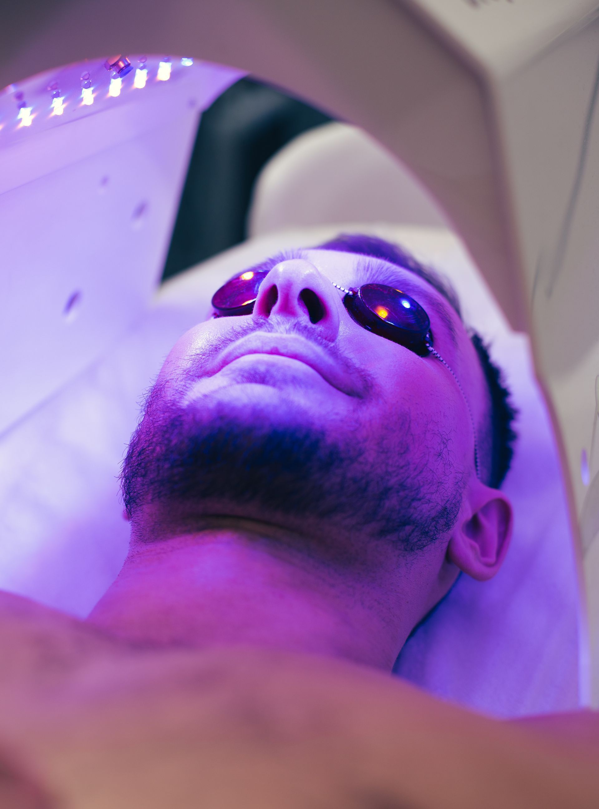 A man is getting a purple light treatment on his face.