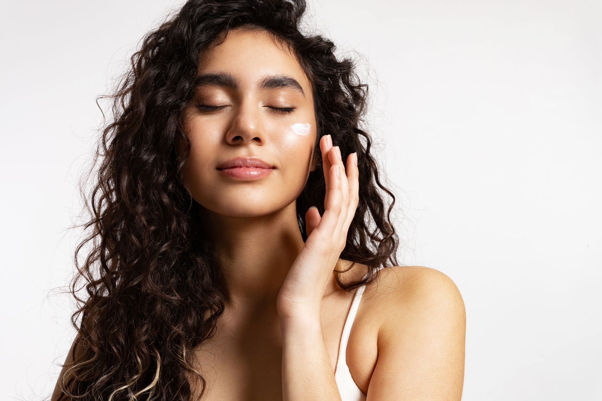 Woman with curly hair, eyes closed, touching her face against a white background