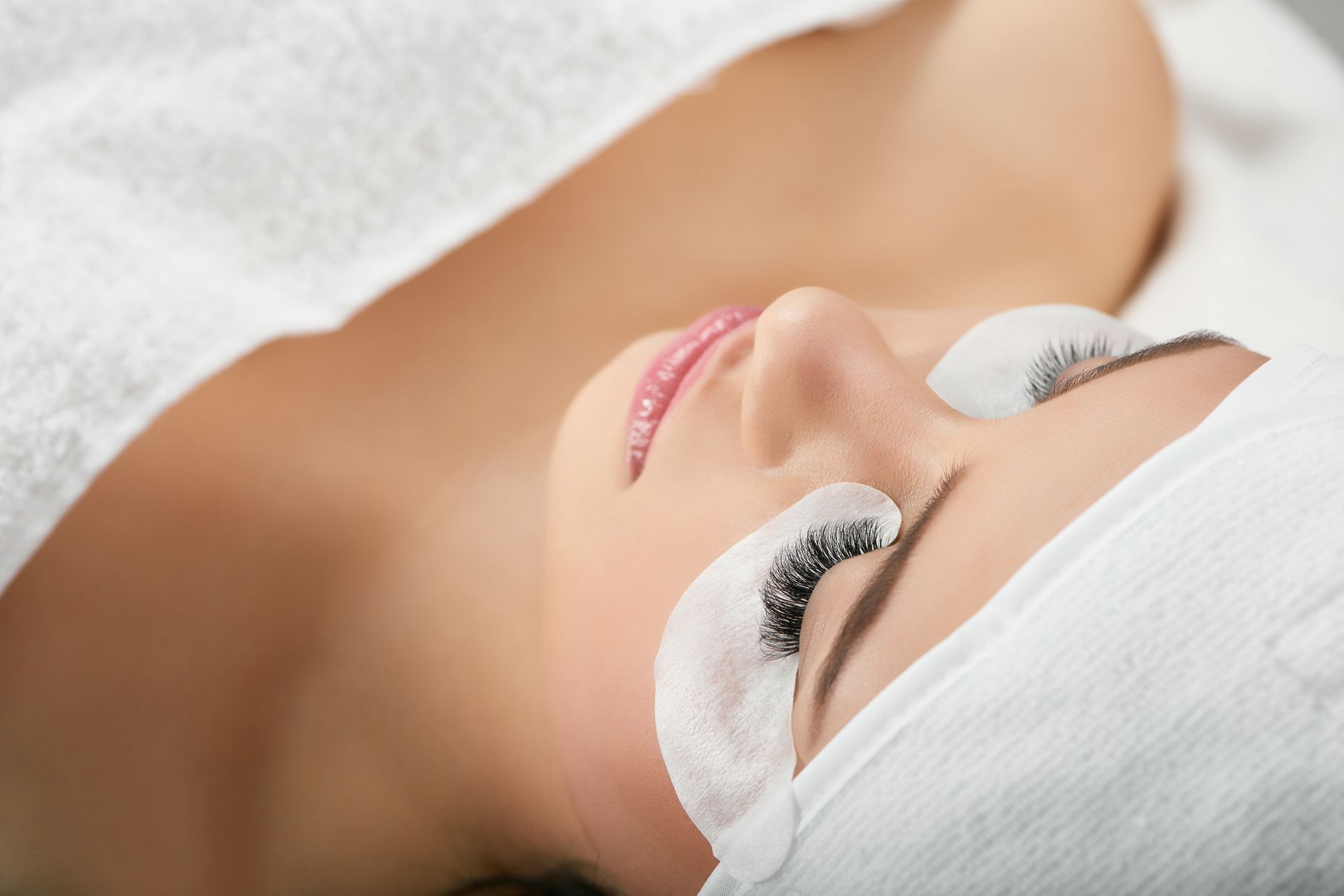 A woman is laying on a bed with a white towel on her head.