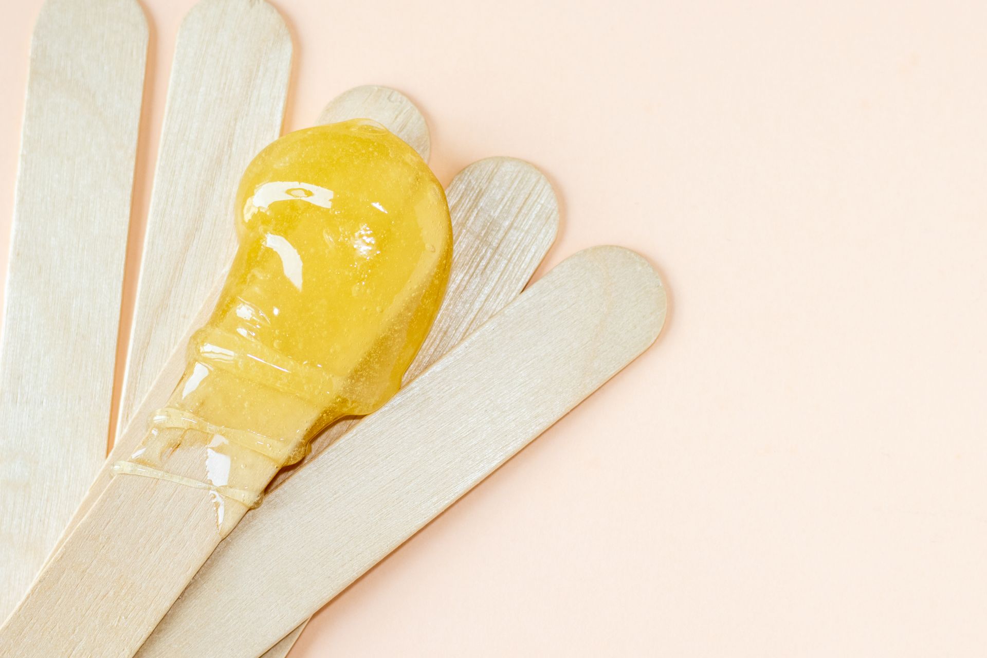 A close up of wax on wooden sticks on a pink background.