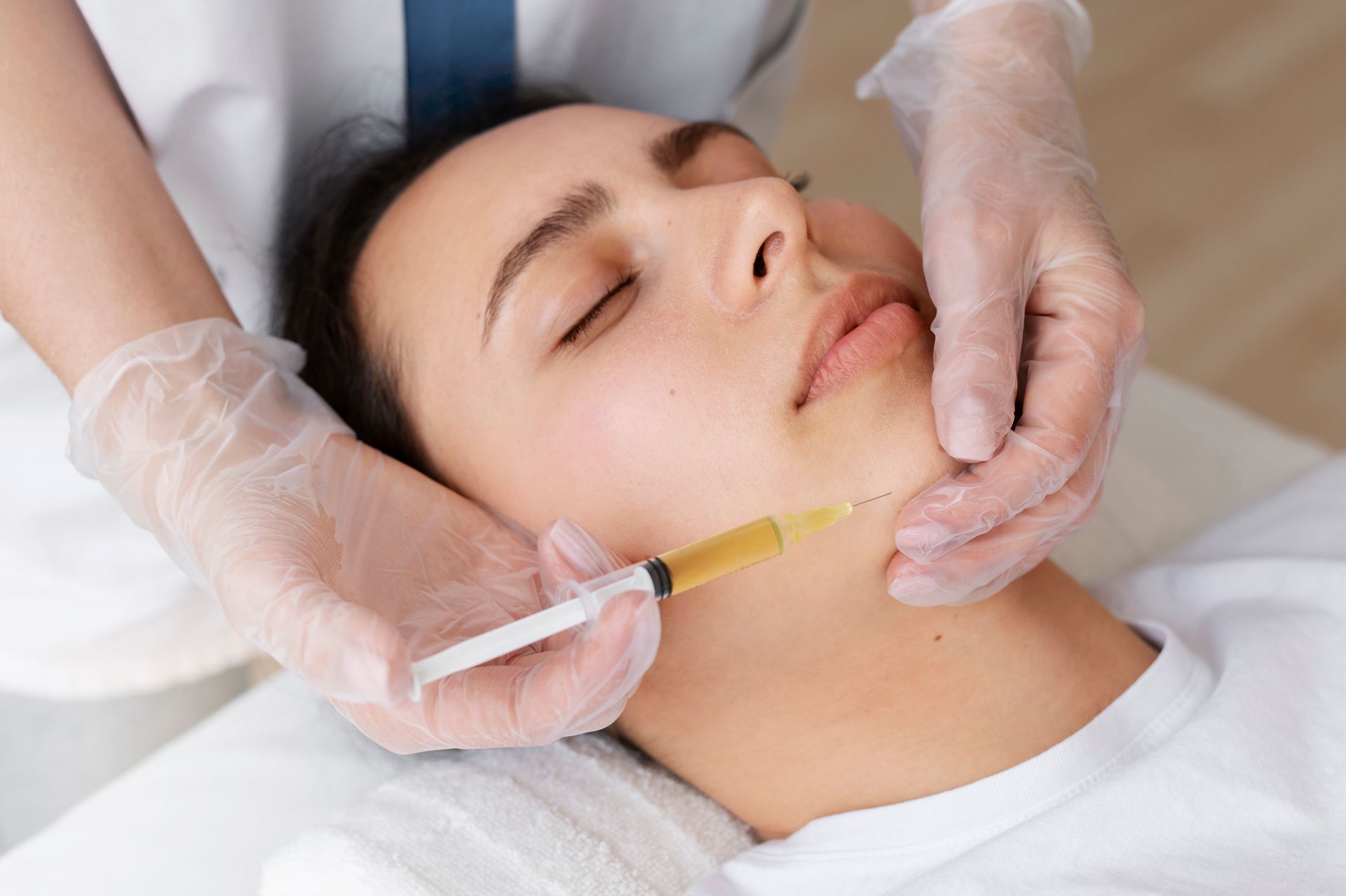 Woman receiving a facial injection with gloved hands in a medical setting.