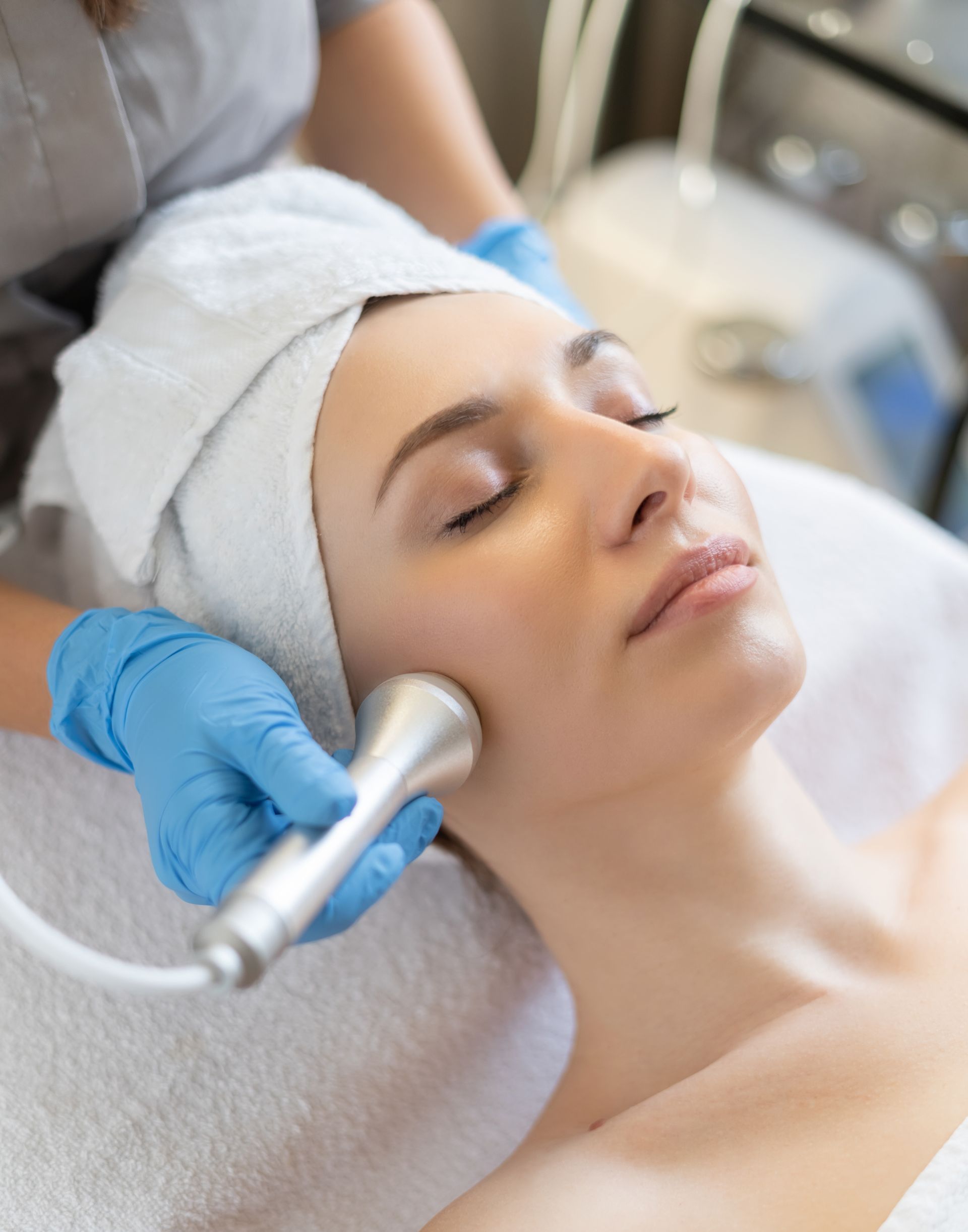 A woman with a towel wrapped around her head is getting a facial treatment.