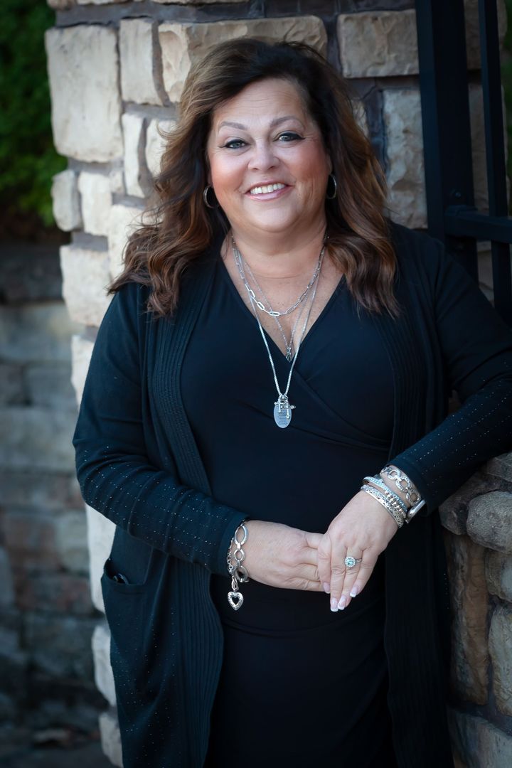 A woman in a black dress and cardigan is standing in front of a stone wall.