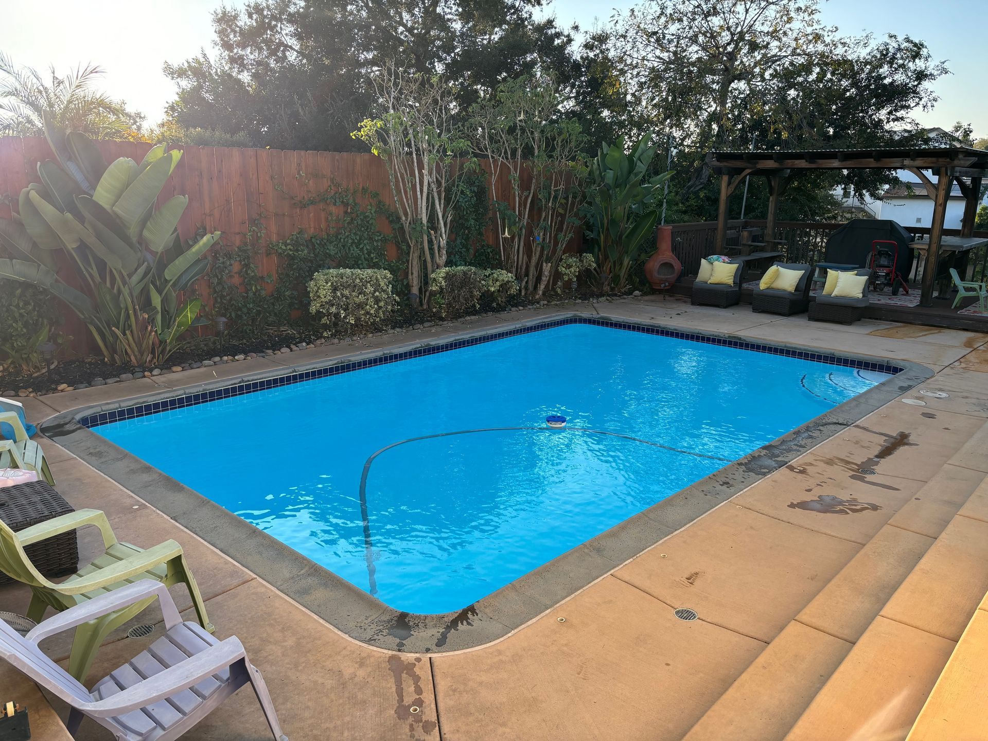 A large swimming pool in a backyard with chairs and a pergola.