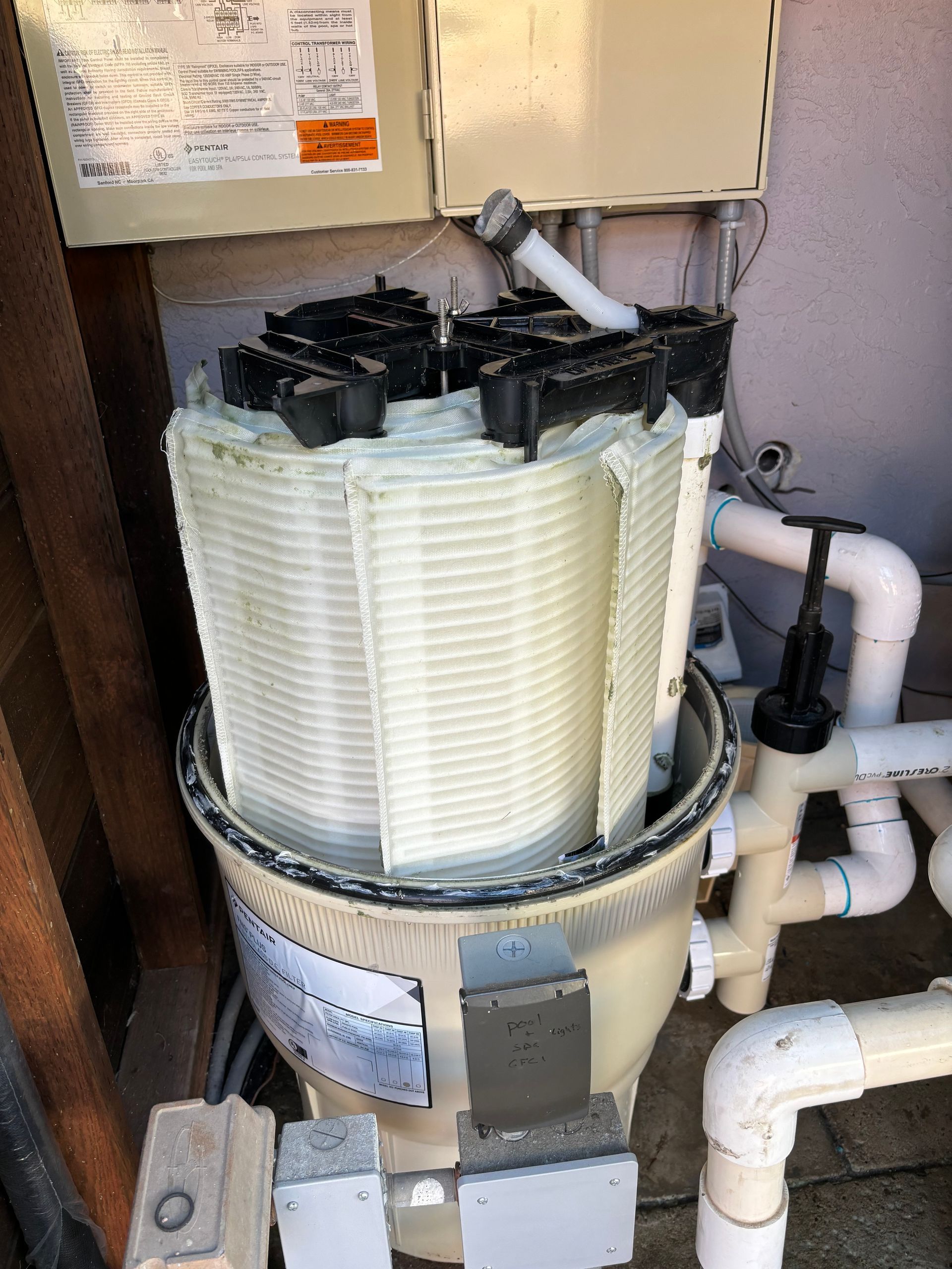 A swimming pool filter is sitting on the ground next to pipes.