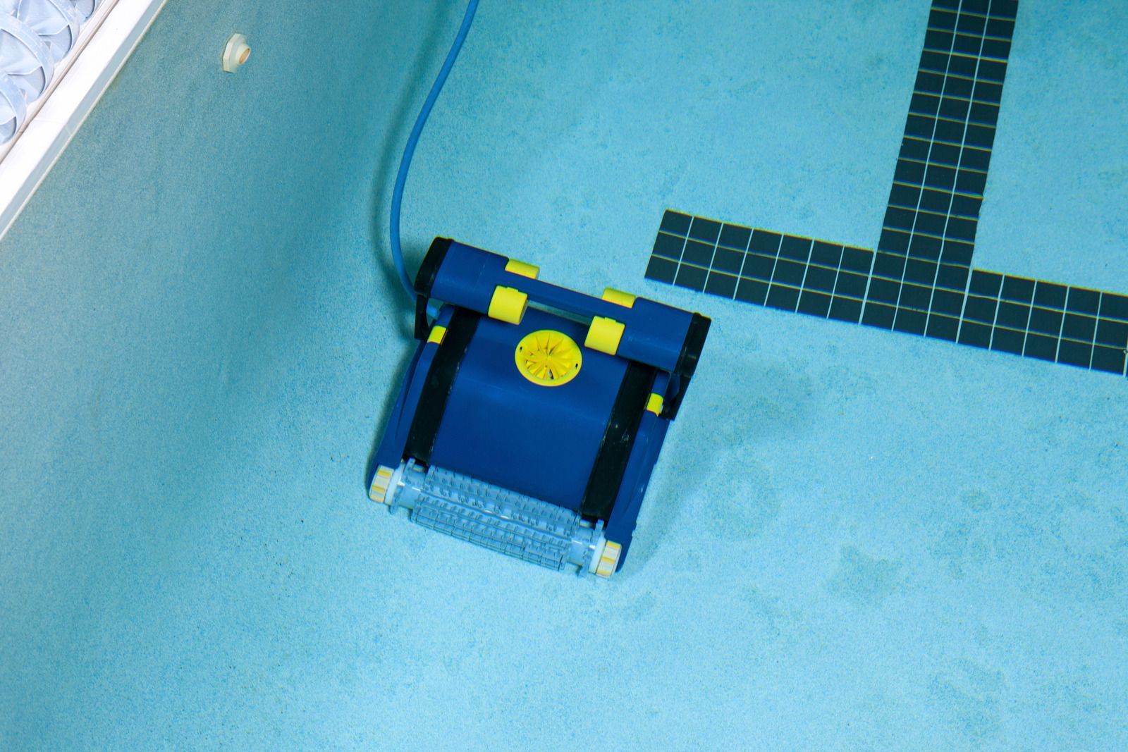 A blue and yellow robot is sitting on the floor of a swimming pool