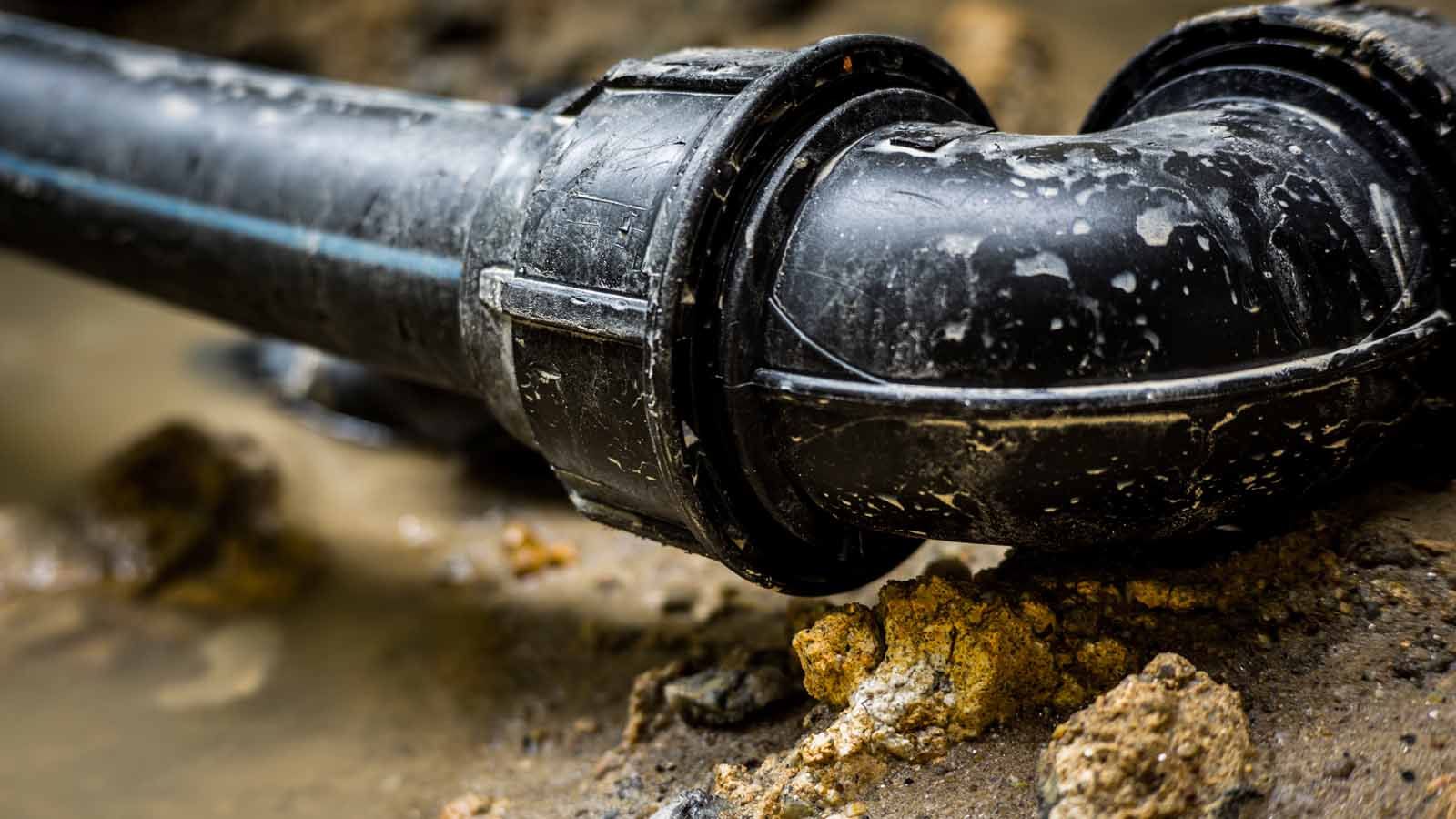 Black plastic drainage pipe elbow on wet ground with water stains and dirt debris