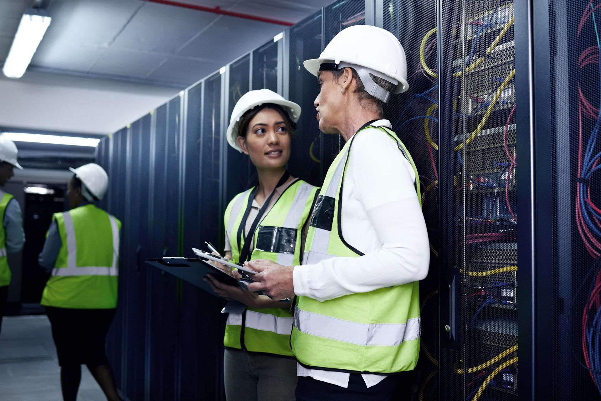 Data center technicians in hard hats and vests inspecting server racks.