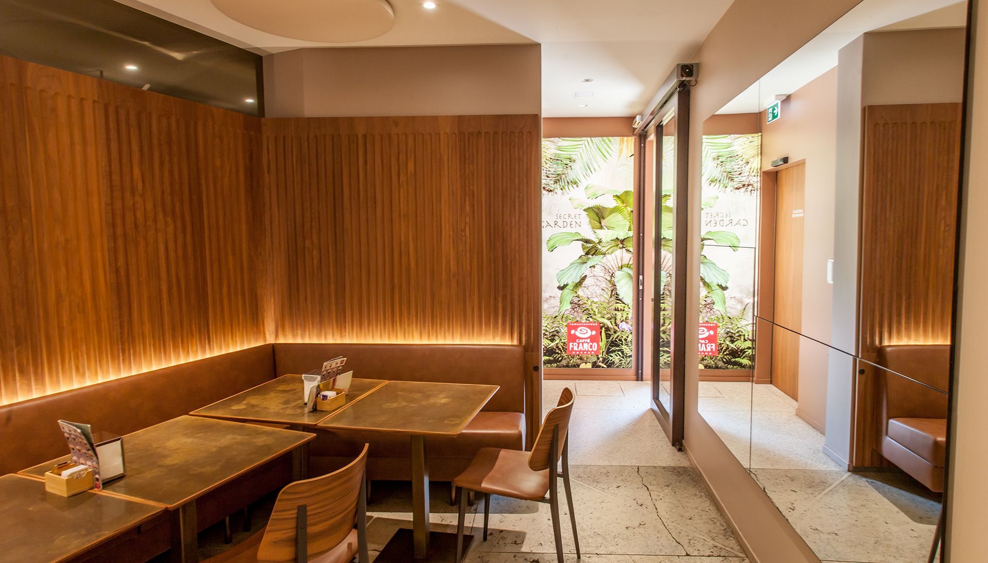 Sala da pranzo moderna del ristorante con tavoli in legno, luci soffuse e porta aperta su un patio con giardino.