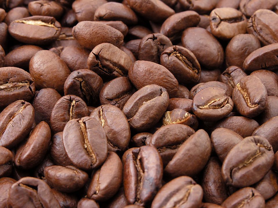 Primo piano di chicchi di caffè tostati che riempiono l'inquadratura, mostrando la loro texture marrone lucida e le crepe.