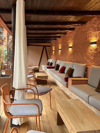 Salotto in legno con divani e poltrone beige e luci a parete dai toni caldi lungo una lunga terrazza simile a un corridoio.